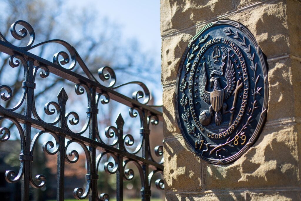 Photo of Georgetown's seal in dark iron on a sandstone wall next to a strong wrought iron gate.